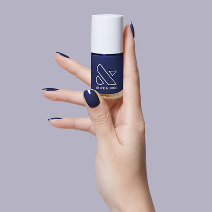 Hand holding OMG polish bottle with nails painted in deep indigo for a smooth, long-lasting manicure by Olive and June