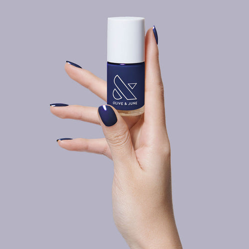 Hand holding OMG polish bottle with nails painted in deep indigo for a smooth, long-lasting manicure by Olive and June