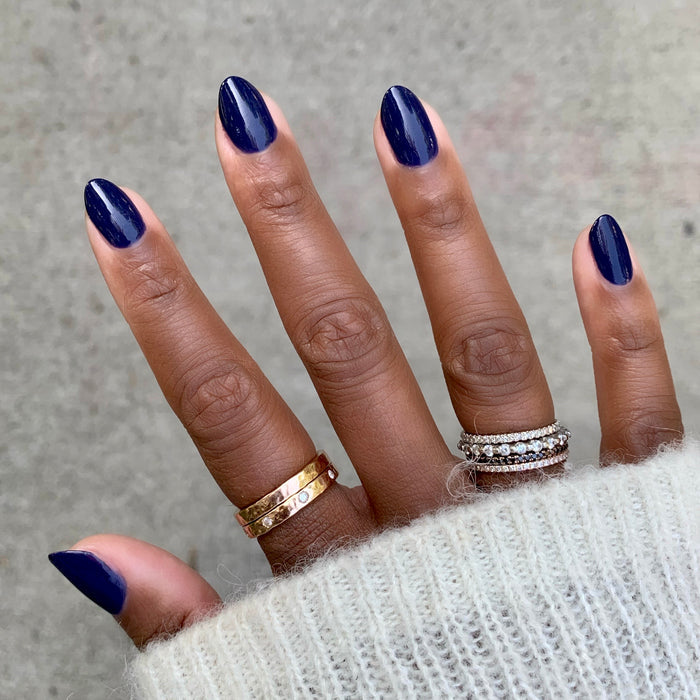 Hand with nails painted in glossy deep indigo OMG polish showing a smooth, long-lasting manicure with a cozy sweater sleeve