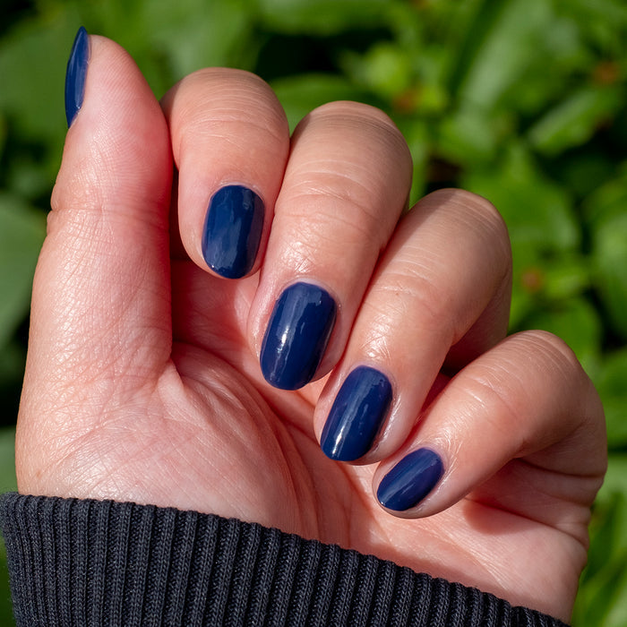 Fingernails painted with smooth, deep indigo OMG polish for a stylish, long-lasting manicure in natural light