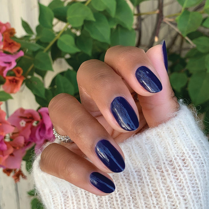 Hand with nails painted glossy, deep indigo OMG polish showing a smooth, long-lasting manicure in natural light