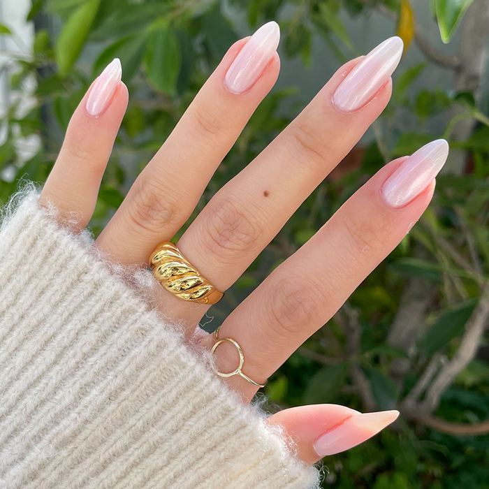 Pearl Polish Set featuring neutral pink nails with a pearlescent shimmer on long, almond-shaped nails with gold rings