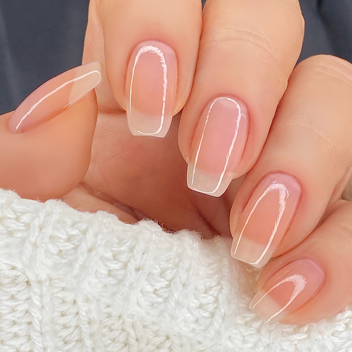 Pure sheer pink peach nail polish close-up on a light skin tone with a white sweater