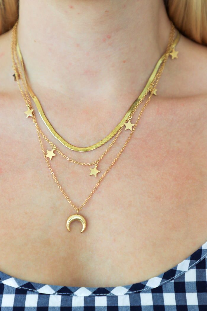Close-up of a person wearing gold necklaces with star and moon pendants.