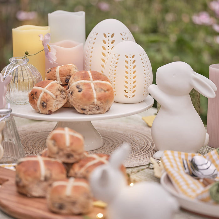 Hot cross buns on an outdoor table with porcelain bunny and easter egg decorations