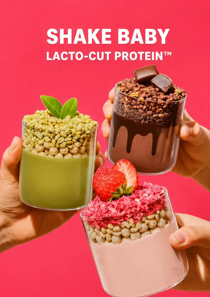 Three hands hold up three different protein shake parfaits against a bright pink background with the text 'SHAKE BABY LACTO-CUT PROTEIN' at the top. The left shake is green with green flakes and a mint leaf, the middle-right shake is dark brown chocolate with chocolate drizzle and a chocolate piece, and the bottom shake is light pink with pink flakes and a strawberry.