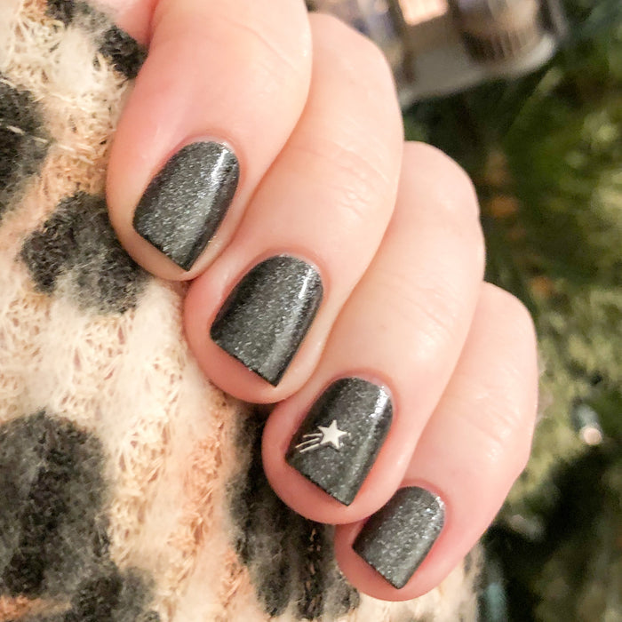 Hand with nails painted in SPACEY showing black shimmer gel polish with star detail and a smooth, long-lasting manicure finish