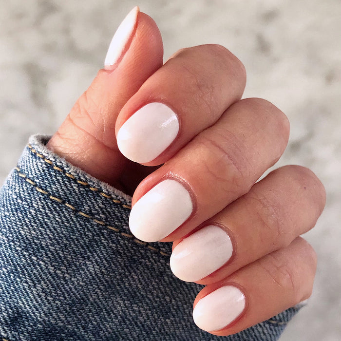 Hand with nails coated in STELLAR polish showing a smooth, shimmering white manicure with salon-quality finish