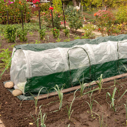 A green poly tunnel covers over a garden bed, protecting young plants, with visible earth pegs and drawstrings securing it to the ground.