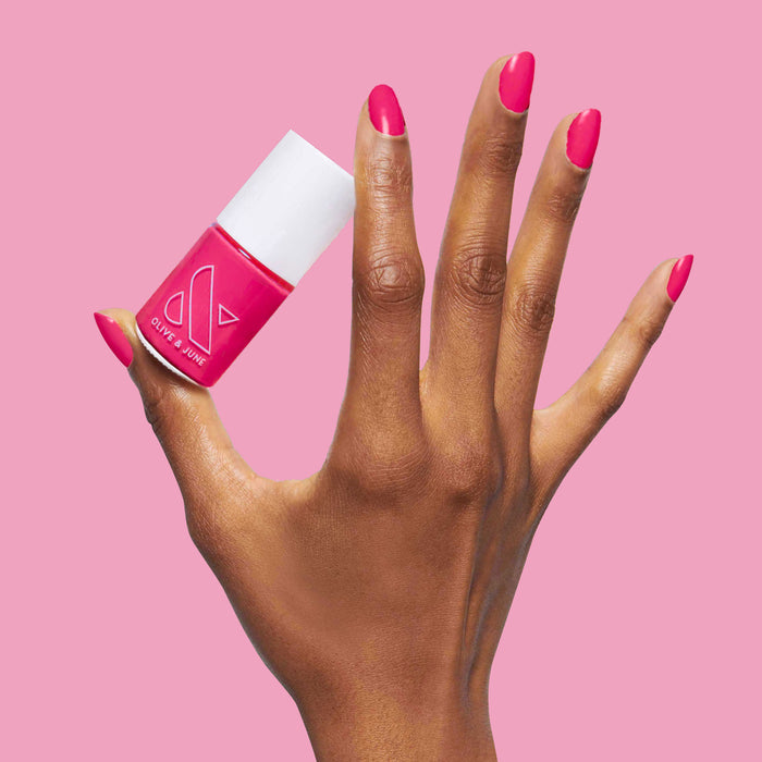 Hand with bright pink XOXO nail polish applied holding matching polish bottle against pink background