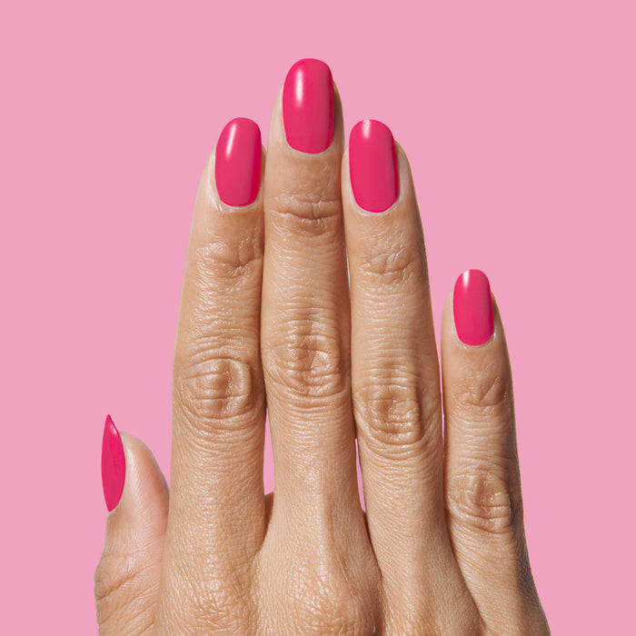 Hand with nails painted in bright hot pink XOXO polish on a matching pink background for a bold mani look
