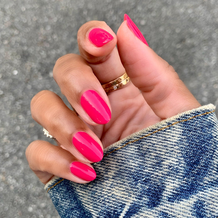 Hand with smooth nails painted in vibrant hot pink XOXO polish against a gray outdoor background for manicure inspiration
