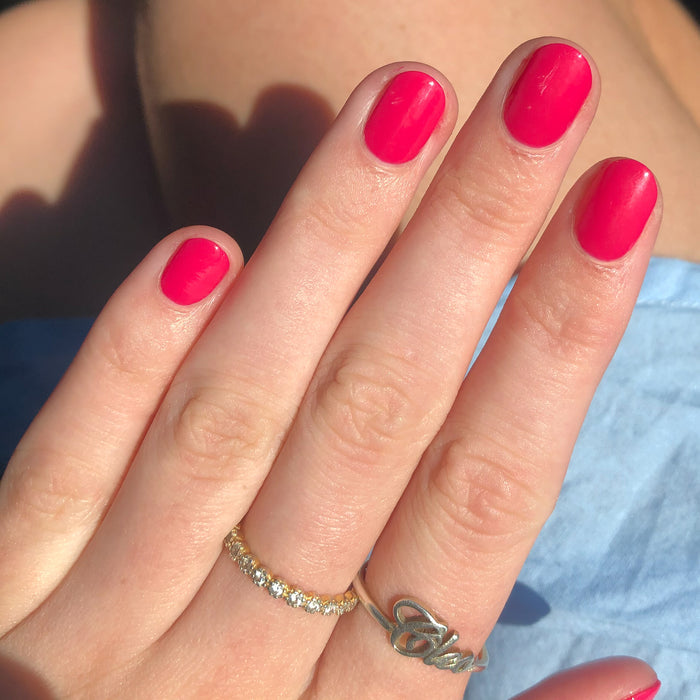 Hand with nails coated in glossy XOXO polish in bright hot pink showcasing a smooth, long-lasting manicure outdoors