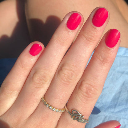 Hand with nails coated in glossy XOXO polish in bright hot pink showcasing a smooth, long-lasting manicure outdoors
