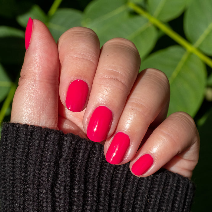 Hand displaying smooth nails painted with XOXO hot pink polish for a bright, long-lasting manicure outdoors